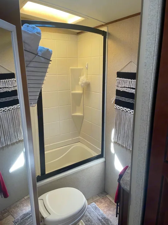 Compact RV rental bathroom: features a toilet, shower/tub, and a modern macrame wall hanging. Bright and clean.. Forest River Surveyor 2014