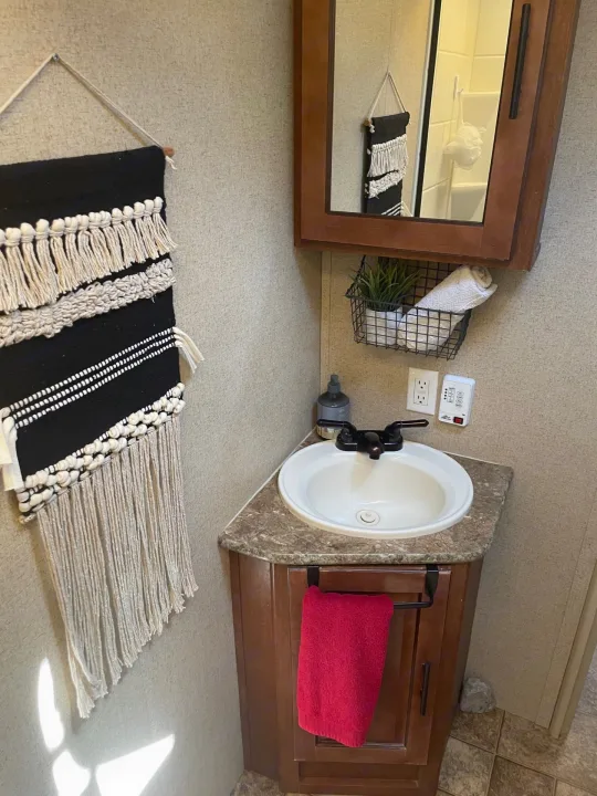 Inside an RV rental: a cozy bathroom with a corner sink, mirror, and unique macrame wall art.. Forest River Surveyor 2014
