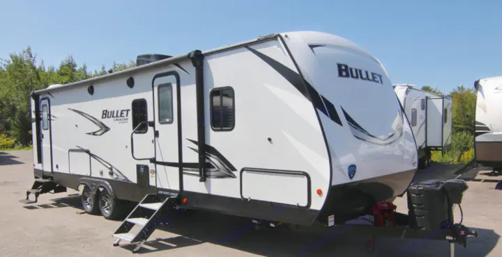 A white "Bullet" travel trailer with black accents and extended steps, parked outdoors. Perfect for your next rv rental and camping trip.. Keystone RV Bullet Ultra Lite 2021