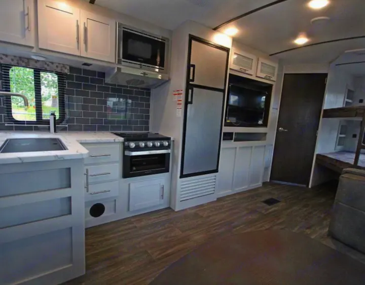 RV rental interior showcasing a modern kitchen with gray subway tile, full-size fridge, TV, and rear bunk beds. Ideal for trips.. Keystone RV Bullet Ultra Lite 2021