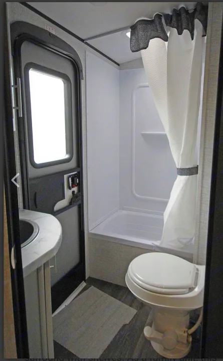 Compact RV rental bathroom showcasing shower/tub, toilet, sink, and exit door with window.. Keystone RV Bullet Ultra Lite 2021