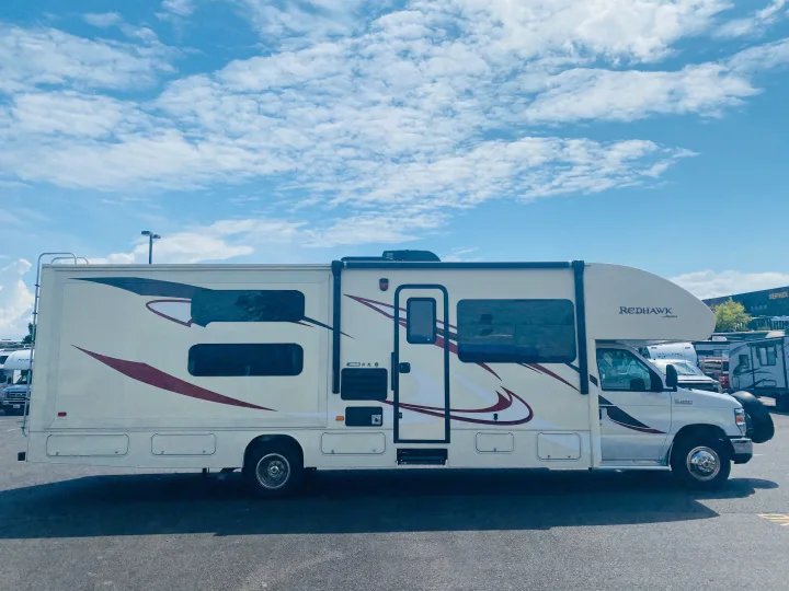 Side view of a white Jayco Redhawk Class C **rv rental** with a slide-out extended, parked on asphalt under a cloudy sky.. Jayco Redhawk 2016
