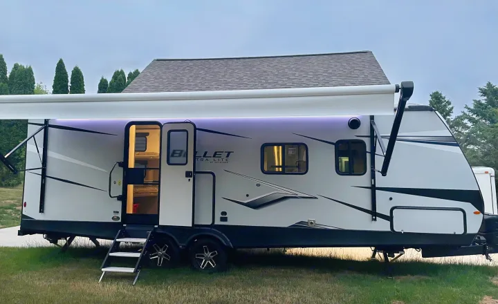 Relax under the illuminated awning of this modern RV rental travel trailer, parked on grass for a serene outdoor evening.. Keystone RV Bullet Ultra Lite 2022