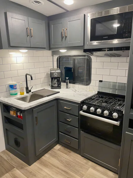 Modern RV rental kitchen with grey cabinets, white subway tile backsplash, and modern appliances.. Keystone RV Bullet Ultra Lite 2022