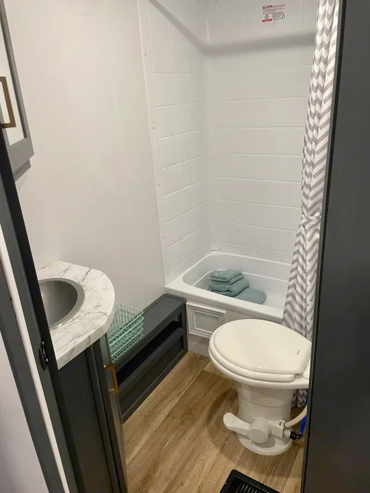 RV rental bathroom: white shower/tub, toilet, vanity with sink, and chevron shower curtain.. Keystone RV Bullet Ultra Lite 2022