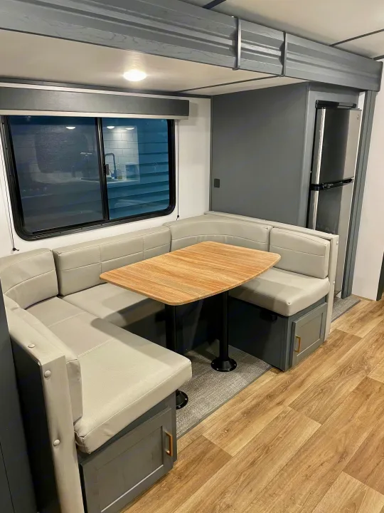 RV rental dinette: light gray U-shaped seating, wood-toned table, window, and kitchen view. Features modern decor.. Keystone RV Bullet Ultra Lite 2022
