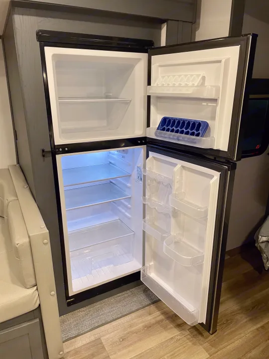 An empty, compact refrigerator with open doors, showing freezer & fridge sections, typical for an rv rental.. Keystone RV Bullet Ultra Lite 2022