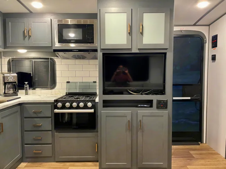 RV rental: Modern gray kitchen and living area featuring stove, microwave, TV, and cabinetry.. Keystone RV Bullet Ultra Lite 2022