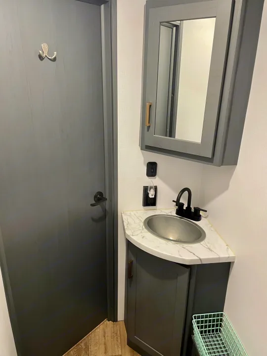 RV rental bathroom with a corner vanity, sink, mirrored cabinet, and a grey door featuring an octopus hook.. Keystone RV Bullet Ultra Lite 2022