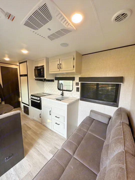 This bright rv rental interior features a modern kitchen, comfy sofa, and clean wood-look flooring, offering comfort.. Jayco Jay Flight SLX 2022