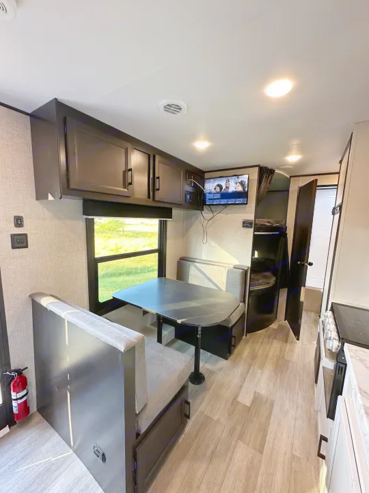 Inside this modern RV rental: a bright dinette area, overhead cabinets, wall-mounted TV, kitchen, and bunk beds.. Jayco Jay Flight SLX 2022