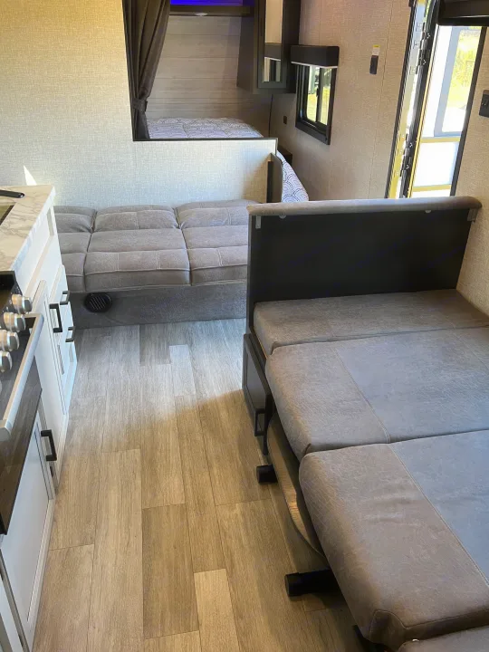 RV rental interior showing the living area with multiple grey convertible sofas, a kitchen, and a bunk bed.. Jayco Jay Flight SLX 2022