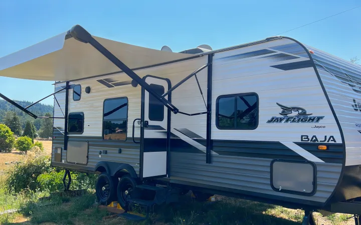 This Jayco Jay Flight travel trailer, ideal for an RV rental, shows its extended awning under blue skies.. Jayco Jay Flight SLX 2022