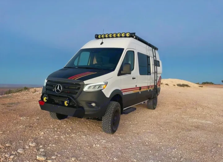 A custom white/black Mercedes Sprinter camper van, equipped for off-road rv rental trips, on a gravelly desert overlook.. Mercedes-Benz sprinter 2023
