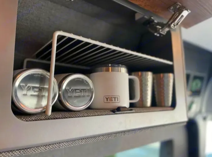 RV rental overhead cabinet with a wire shelf holds YETI cans, mugs & cups. Smart, organized storage for travel.. Mercedes-Benz sprinter 2023