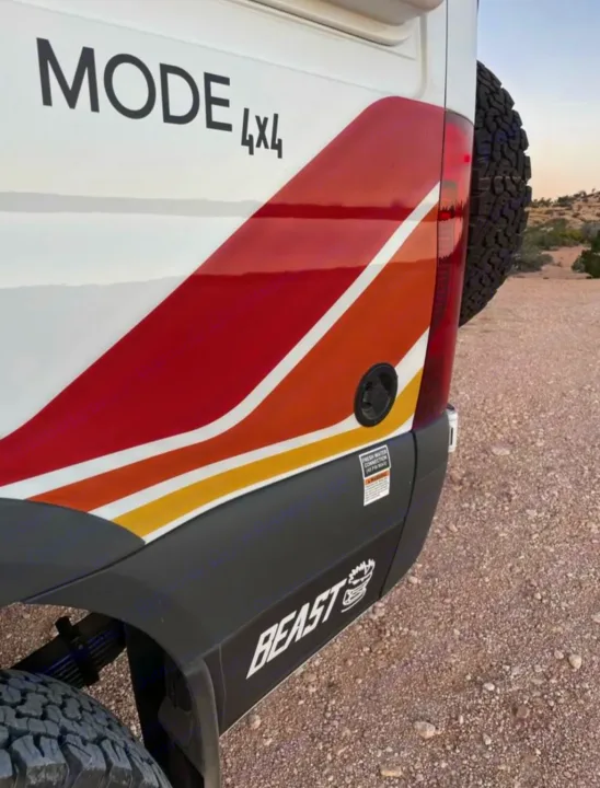 Rear view of a white MODE 4x4 rv rental camper van with retro red/orange/yellow stripes and 'BEAST' branding for off-road travel.. Mercedes-Benz sprinter 2023