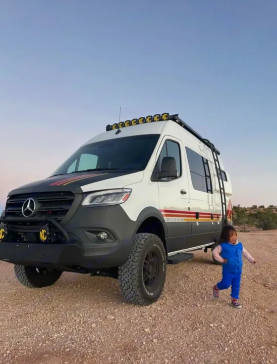 Off-road Mercedes Sprinter **RV rental** for adventure! A child plays near this rugged camper van on a dirt road.. Mercedes-Benz sprinter 2023