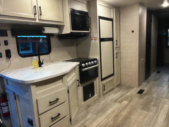 Bright and modern rv rental kitchen area with light cabinets, counter, sink, stove, microwave, and fridge.. Jayco Jay Flight 2023