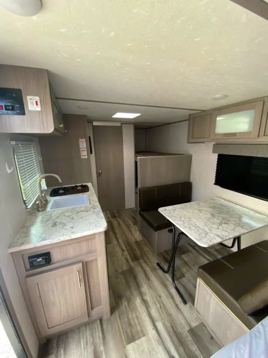 Modern rv rental interior: kitchen with marble counters, dining area, & bunk beds. A clean, functional living space.. Dutchmen Coleman Lantern LT 2023