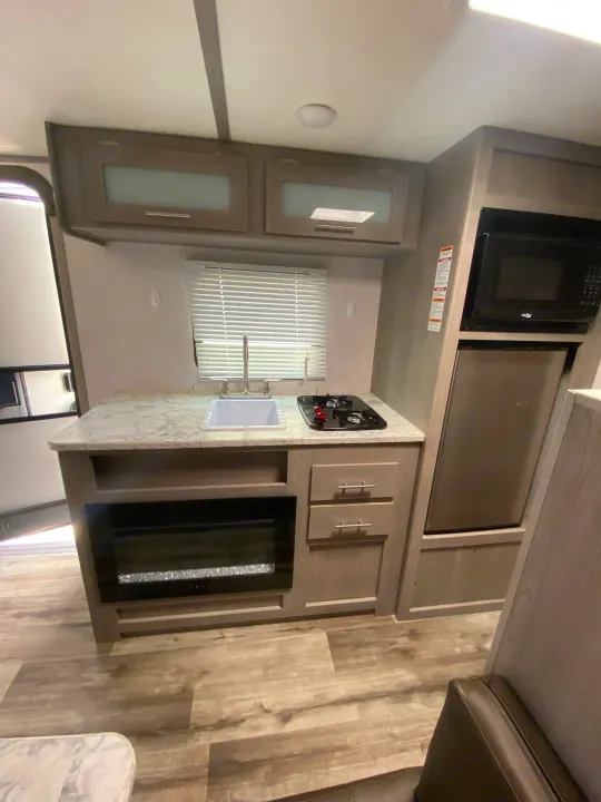 Modern RV rental with a compact kitchenette, featuring a sink, stovetop, microwave, refrigerator, and an electric fireplace.. Dutchmen Coleman Lantern LT 2023