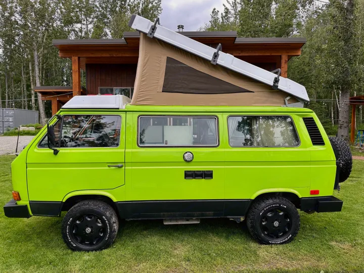 Bright green VW Vanagon camper van with pop-top roof and rugged tires, ready for RV rental adventures.. Volkswagen Westfalia 1984