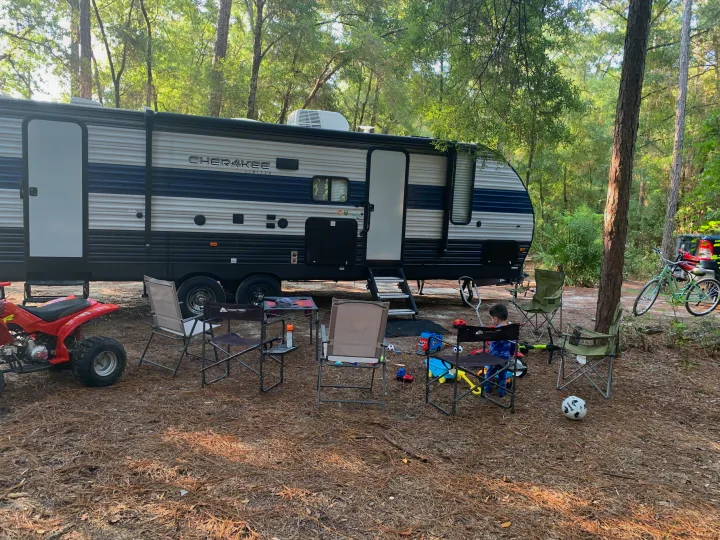Family enjoying a serene campsite with their RV rental, complete with toys, chairs, and an ATV for outdoor fun.. Forest River Cherokee Grey Wolf 2020