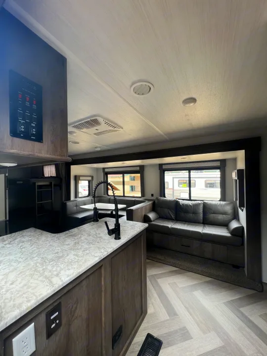Spacious RV rental interior with a bright living area, kitchen island, dining booth, sofa, and bunk beds.. Forest River Wildwood 2021