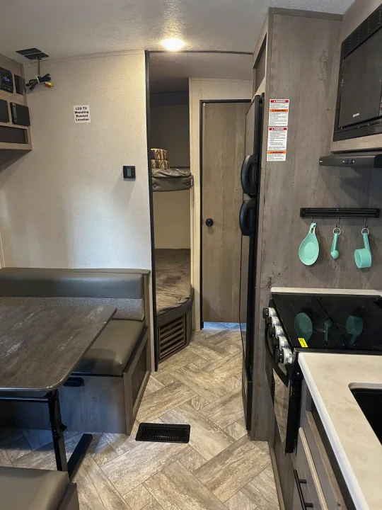 Explore this RV rental's compact interior featuring a dinette, kitchen with stove, and bunk area visible down the hall.. Keystone RV Springdale 2021