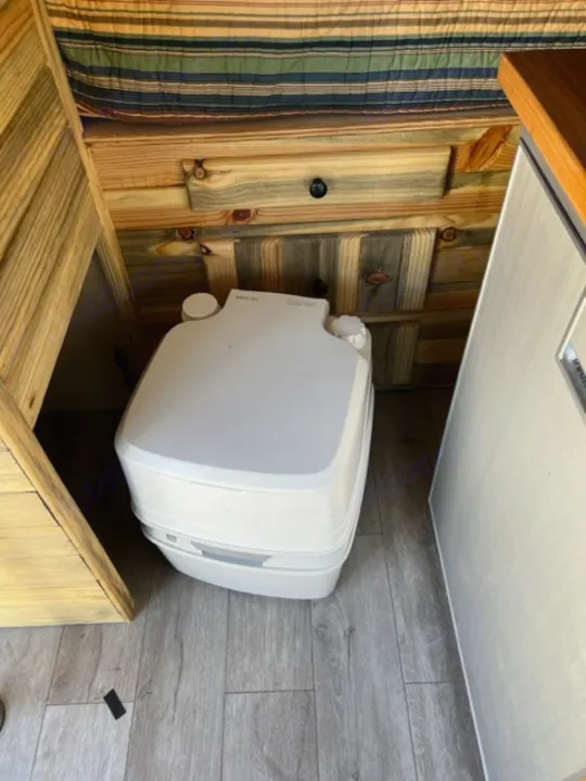 RV rental interior: A portable toilet, wooden walls, and striped bedding in a compact space.. Ford Transit 2015