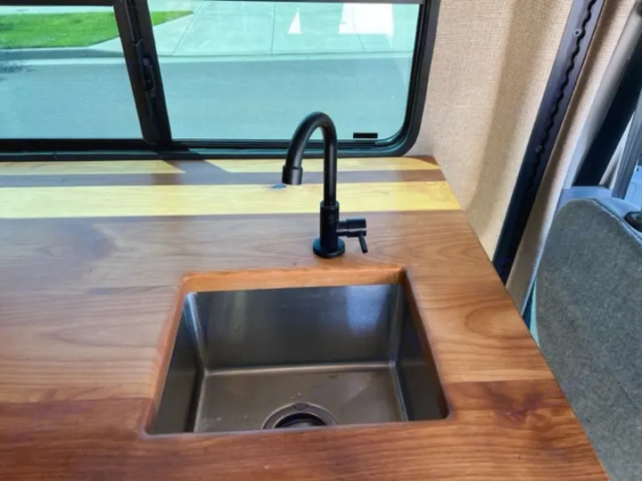 Modern rv rental interior featuring a wood countertop, sleek sink, and black faucet. Perfect for road trips!. Ford Transit 2015