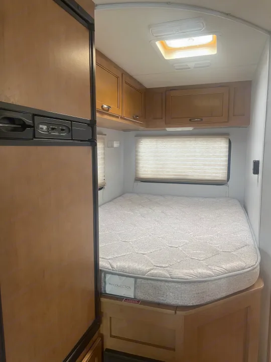 RV rental bedroom view: comfortable bed with an RV Collection mattress, overhead cabinets, and a bright skylight.. Thor Four Winds 2015