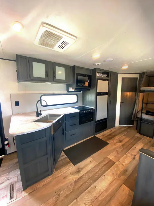 This modern RV rental features a well-equipped kitchen with sink, oven, microwave, fridge, and adjacent bunk beds.. Aspen Trail Aspen Trail Trailer 2021