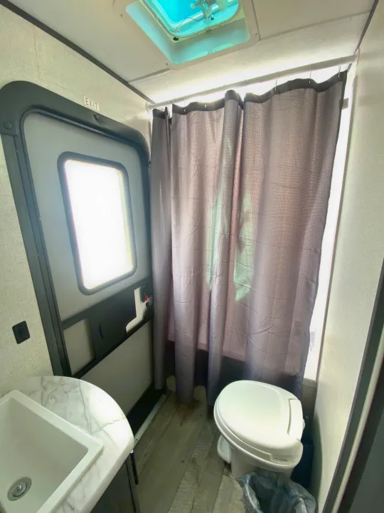 Compact RV rental bathroom showing sink, toilet, shower curtain, and door with EXIT sign.. Aspen Trail Aspen Trail Trailer 2021
