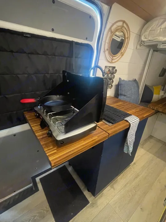 Compact RV rental kitchen in a camper van, featuring a portable stove, sink, and wood countertops, ideal for mobile cooking.. Mercedes Sprinter 2010