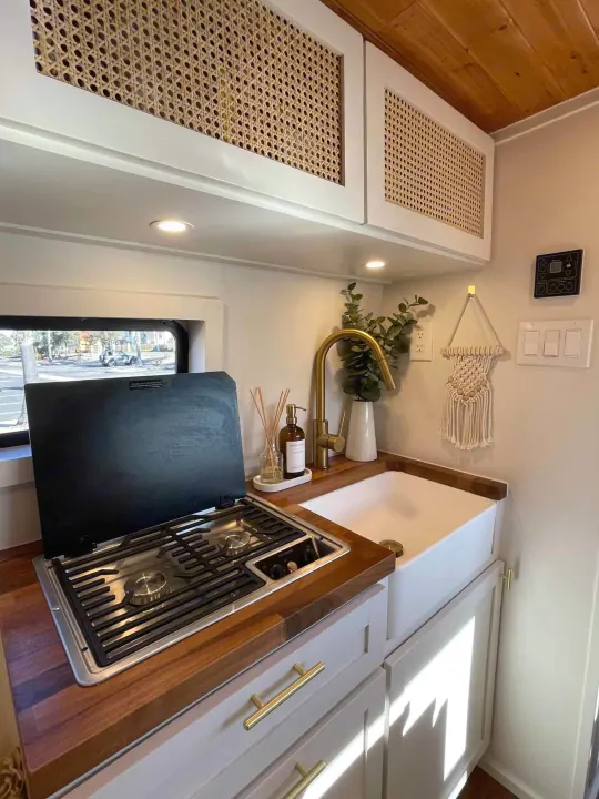 Modern RV rental kitchenette: white cane cabinets, wood counters, 2-burner stove, and farmhouse sink. Bright & functional.. Mercedes-Benz Sprinter 2021