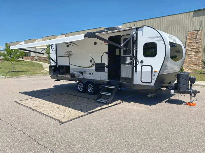 White & gray travel trailer RV rental parked on asphalt with extended awning & outdoor rug. Ready for your camping adventure!. Forest River Rockwood Mini Lite 2021