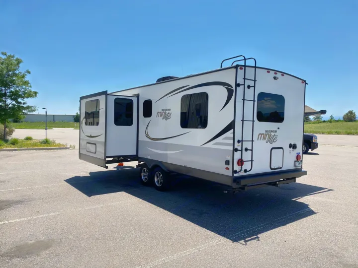 A white Rockwood Mini Lite travel trailer, ideal for an RV rental, with its slide-out extended, parked on a sunny day.. Forest River Rockwood Mini Lite 2021