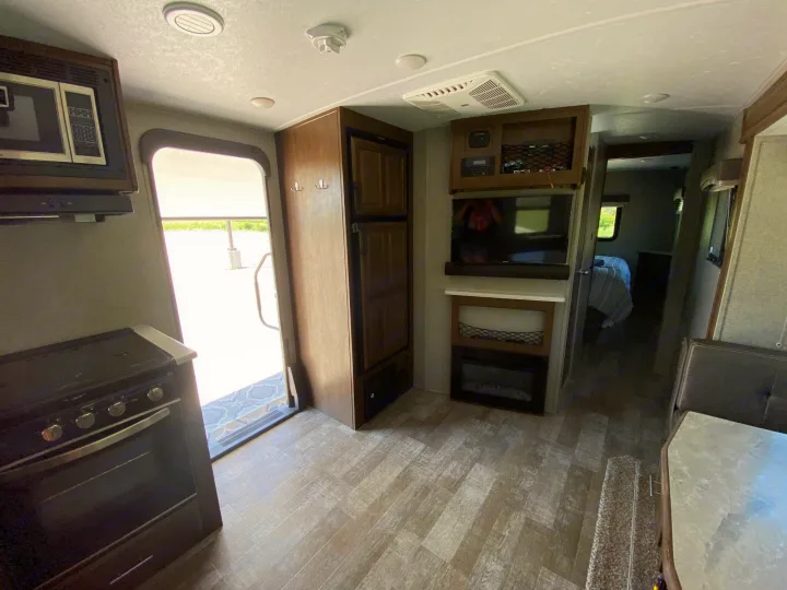 Interior view of an RV rental, featuring a kitchen (microwave, stove), living area with entertainment center, fridge, & bedroom access.. Forest River Rockwood Mini Lite 2021