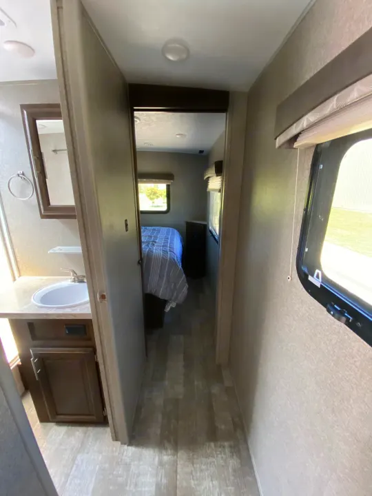 RV rental interior showcasing a compact bathroom with sink, mirror, and a hallway leading to a cozy bedroom with a bed and window.. Forest River Rockwood Mini Lite 2021