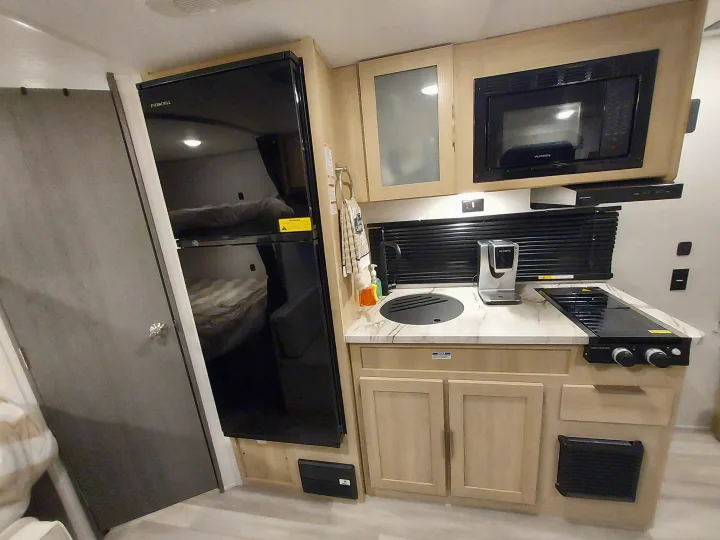 Spacious RV rental kitchen with a large black fridge, microwave, sink, and stovetop. Light wood cabinets and marble counter.. Forest River Salem FSX Platinum 2023