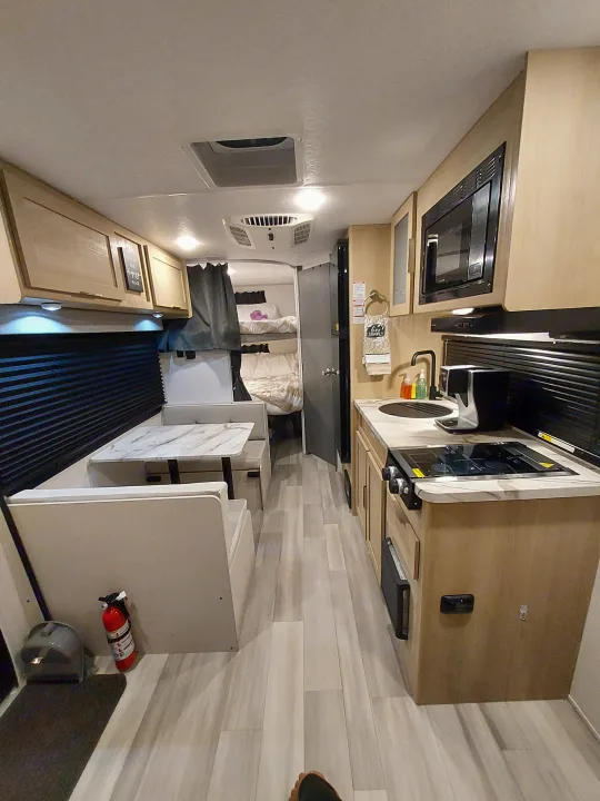 Bright RV rental interior showing a compact kitchenette with microwave, dining area, and rear sleeping space, ideal for travel.. Forest River Salem FSX Platinum 2023