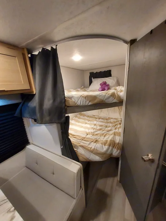 RV rental interior featuring a cozy bed with striped bedding and a purple toy, plus a compact seating area.. Forest River Salem FSX Platinum 2023