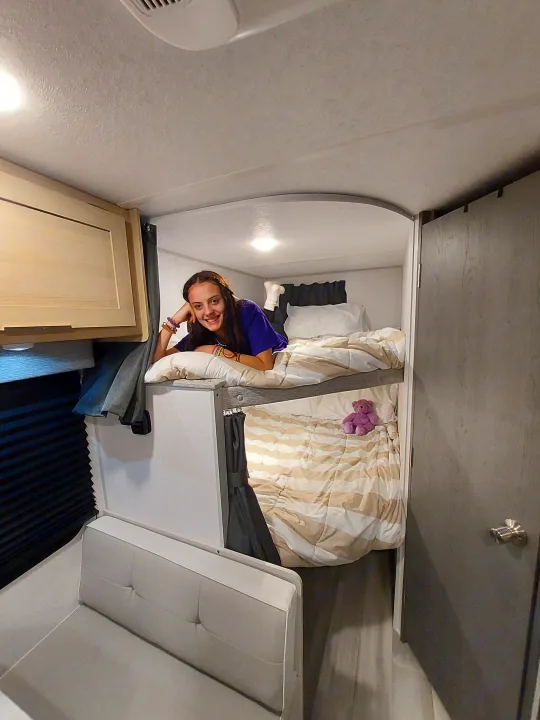 Enjoying a cozy RV rental bed: a young woman smiles surrounded by soft bedding and built-in comforts.. Forest River Salem FSX Platinum 2023