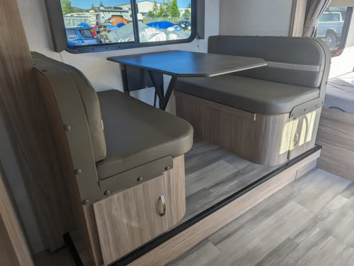 RV rental dinette inside with window view of other campers outside. Features benches, table, and storage.. Winnebago Micro Minnie 2022