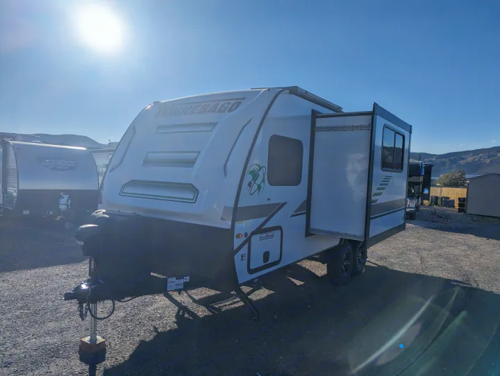 Bright sunny day showcasing a white Winnebago travel trailer, a potential rv rental, with its slide-out extended on a gravel lot.. Winnebago Micro Minnie 2022
