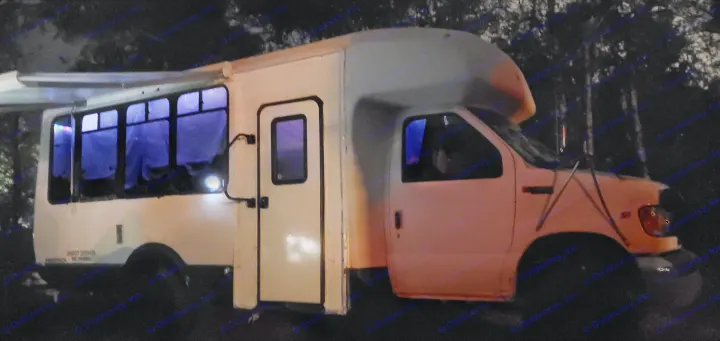 White Ford Econoline converted RV rental at night with glowing purple windows and an open awning.. Ford E450 2000