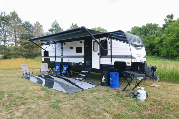 This rv rental features a full outdoor setup with awning, chairs, grill, and rug, ready for camping adventures.. Keystone RV Hideout 2022