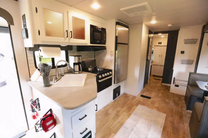 This inviting RV rental interior showcases a modern kitchen with a stove, sink, and fridge, leading to a dining booth.. Keystone RV Hideout 2022