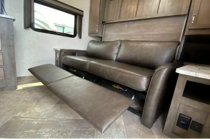Comfortable reclining sofa with extended footrest in an RV rental. Features spacious living area interior.. East to West Alta 2021