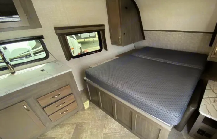 RV rental bedroom area with a comfortable bed, overhead storage, and adjacent kitchen counter.. East to West Alta 2021